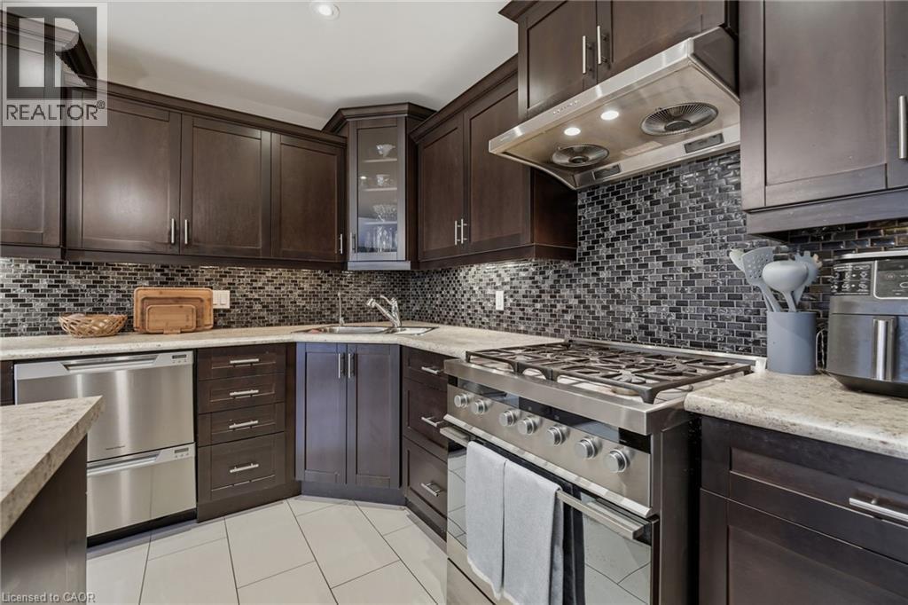 Kitchen featuring dark wood cabinetry, a mosaic tile backsplash, stainless steel appliances, light-toned countertops, and white rectangular floor tiles - 7 Gibson Place Unit# 26, St. Catharines, ON - Indoor Photo Showing Kitchen With Stainless Steel Kitchen With Upgraded Kitchen