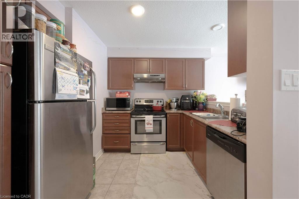 Kitchen with appliances with stainless steel finishes, a textured ceiling, under cabinet range hood, brown cabinets, and light marble finish flooring - 535 Margaret Street Unit# 74, Cambridge, ON - Indoor Photo Showing Kitchen