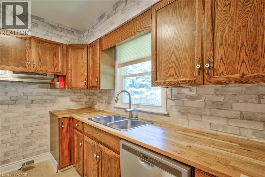 Kitchen featuring wood cabinetry, butcher block countertops, stainless steel double basin sink, stainless steel faucet, and white brick-patterned backsplash - 31 Brodick Street, Hamilton, ON - Indoor Photo Showing Kitchen With Double Sink