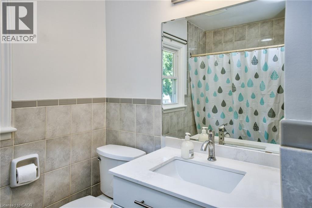 Bathroom featuring a vanity with an integrated sink and light-toned countertop, a polished chrome faucet, a large wall-mounted mirror, and a toilet - 31 Brodick Street, Hamilton, ON - Indoor Photo Showing Bathroom