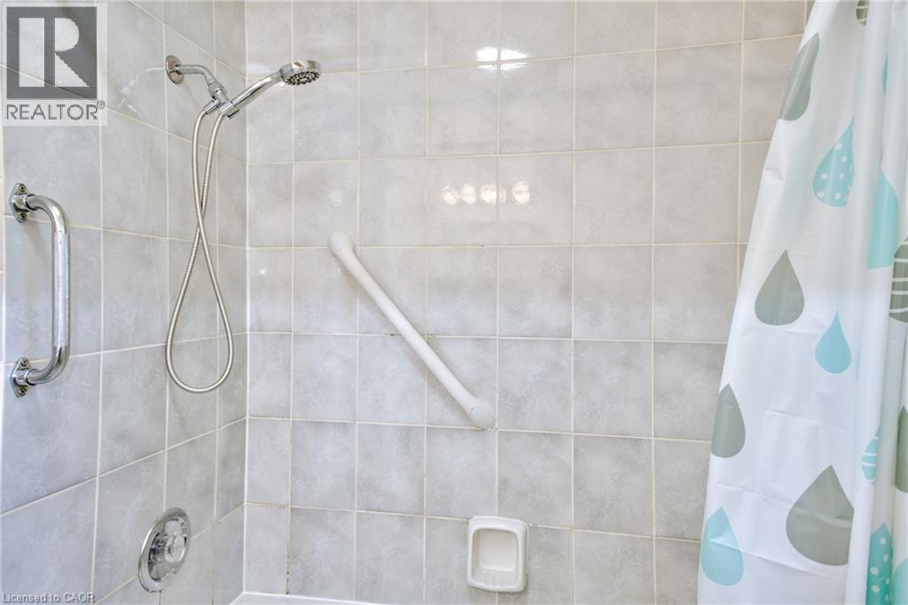 Shower enclosure featuring light-toned square wall tiles, a chrome hand-held showerhead, a chrome wall-mounted grab bar, and a white angled grab bar - 31 Brodick Street, Hamilton, ON - Indoor Photo Showing Bathroom