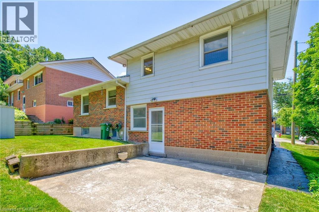 Rear exterior featuring a concrete patio, a concrete retaining wall, and a sloped grass lawn - 31 Brodick Street, Hamilton, ON - Outdoor With Exterior