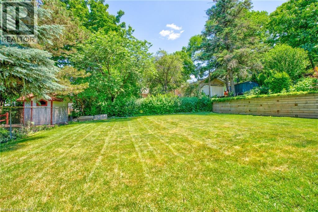 Expansive green lawn surrounded by mature trees, featuring a tiered wood retaining wall and a storage shed - 31 Brodick Street, Hamilton, ON - Outdoor