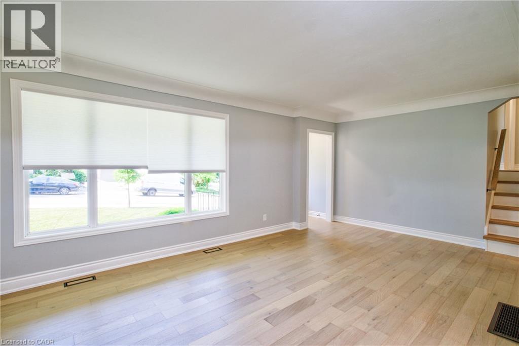 Spacious interior room featuring light wood-finish flooring, a large multi-pane window with white roller shades, and light-toned wall finishes - 31 Brodick Street, Hamilton, ON - Indoor Photo Showing Other Room