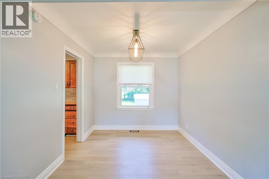 Bright interior space featuring light wood-finish flooring, a contemporary geometric pendant light fixture, and crown molding - 31 Brodick Street, Hamilton, ON - Indoor Photo Showing Other Room