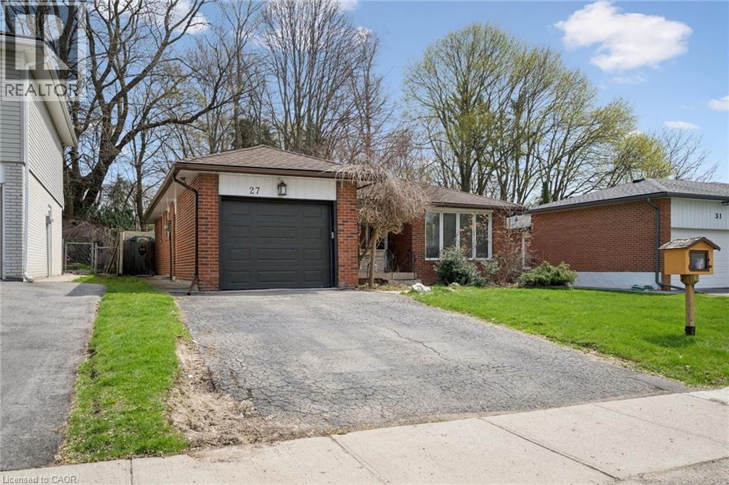 Brick facade home featuring an integrated garage with a dark gray door, a paved driveway, and a front lawn with mature trees - 27 Silverspring Crescent, Kitchener, ON - Outdoor