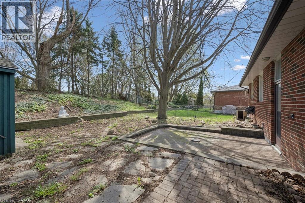 Expansive backyard featuring a brick paver patio, established trees, a sloped natural landscape, and a utility shed - 27 Silverspring Crescent, Kitchener, ON - Outdoor