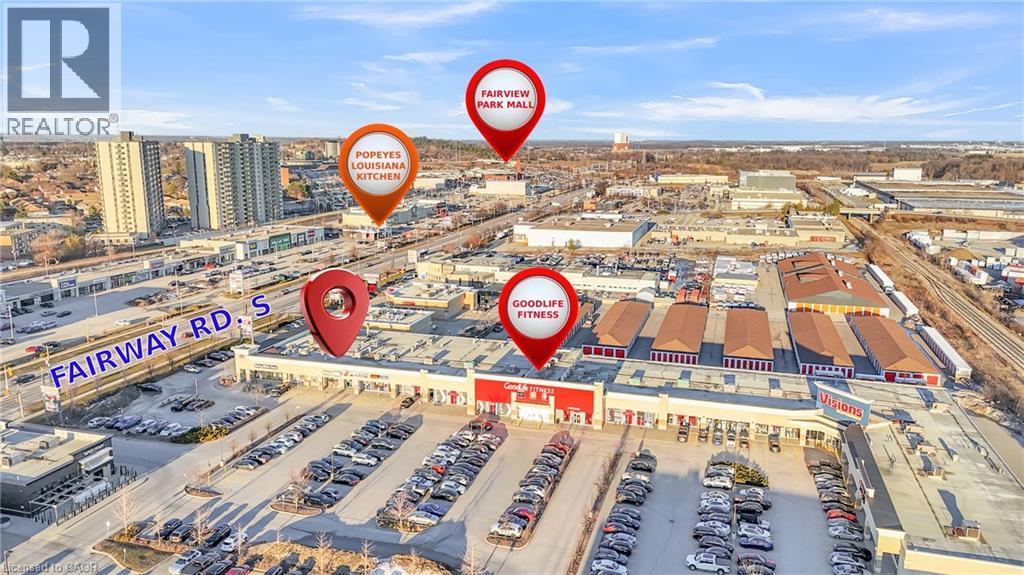 Aerial view highlighting the commercial district with multiple retail establishments, extensive parking areas, and adjacent multi-story residential buildings - 589 Fairway Road S, Kitchener, ON