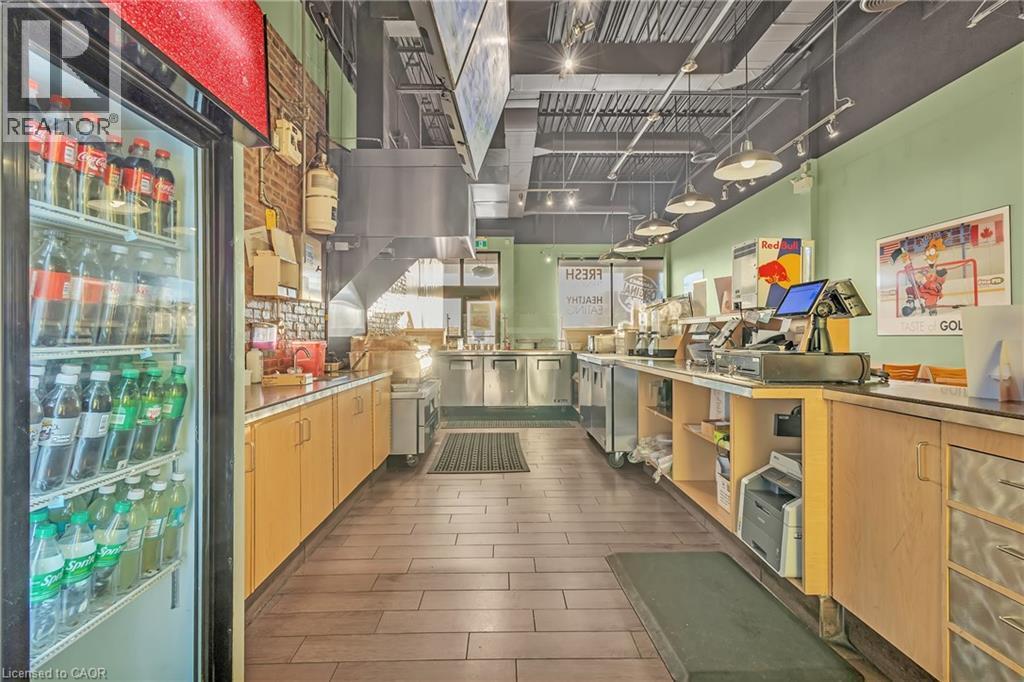 Commercial kitchen area featuring wood-finish flooring, light green walls, exposed brick accents, and a suspended ceiling with track lighting - 589 Fairway Road S, Kitchener, ON
