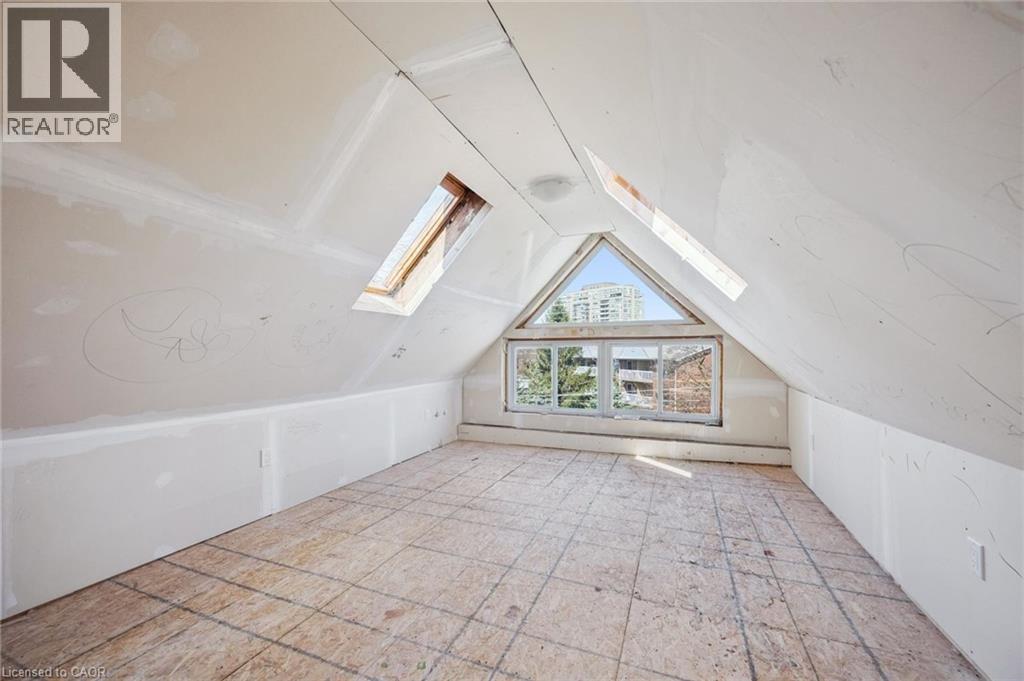 Attic space featuring sloped ceilings, two skylights, a triangular window, and plywood subflooring - 115 Allen Street E, Waterloo, ON - Indoor Photo Showing Other Room