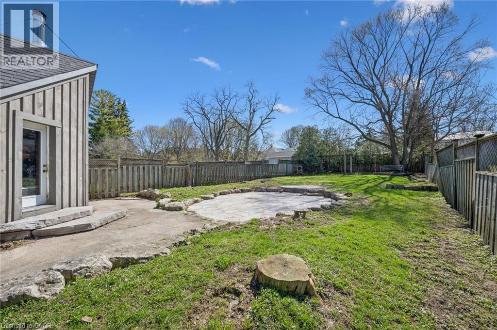 Expansive fenced backyard featuring a stone patio, mature trees, and a board-and-batten exterior wall with a glass-paneled door - 115 Allen Street E, Waterloo, ON - Outdoor With Backyard
