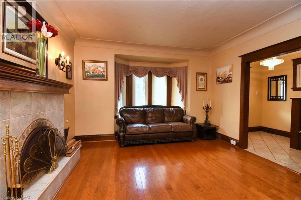 Open concept living space featuring wood-finish flooring, a tiled fireplace with a wood mantel, a bay window with valance, and an arched doorway with wood trim - 522 Aberdeen Avenue, Hamilton, ON - Indoor Photo Showing Living Room With Fireplace