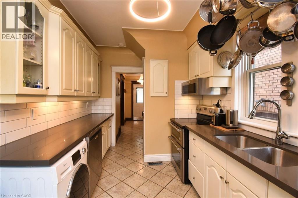 Galley kitchen featuring cream cabinetry, dark countertops, a white subway tile backsplash, stainless steel appliances, and a double basin sink with a gooseneck faucet - 522 Aberdeen Avenue, Hamilton, ON - Indoor Photo Showing Other Room