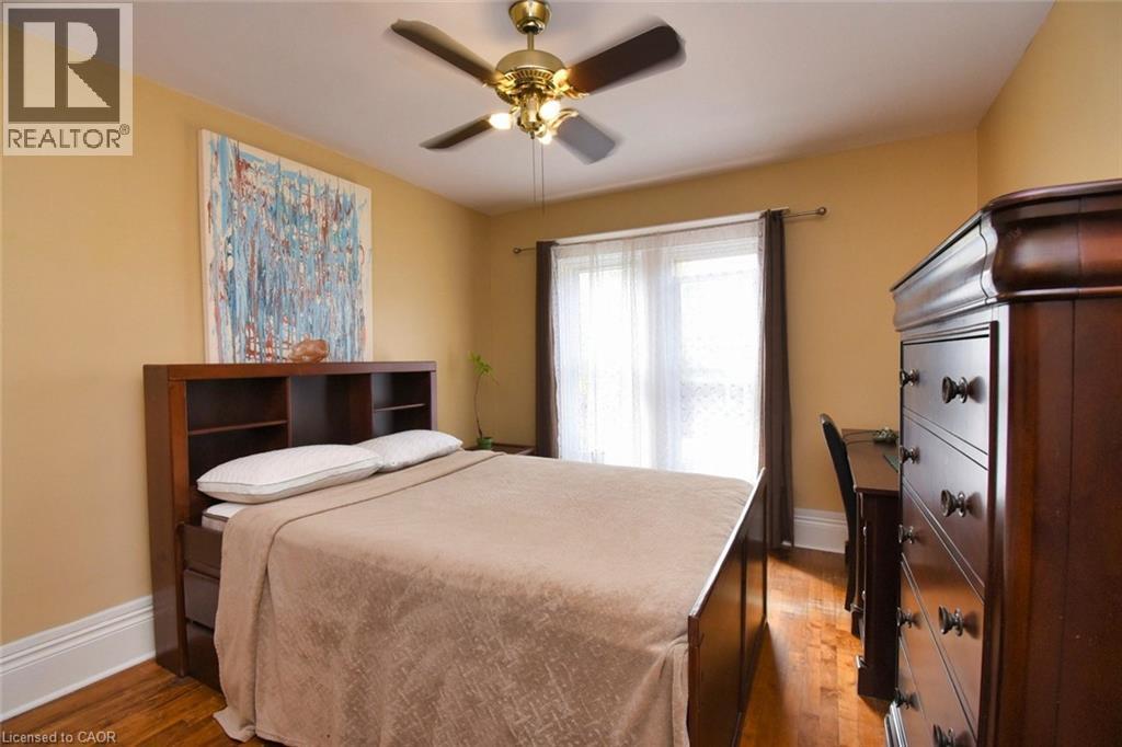 Bedroom featuring warm-toned walls, wood-finish flooring, a ceiling fan with integrated lighting, and a large window with sheer and blackout drapery - 522 Aberdeen Avenue, Hamilton, ON - Indoor Photo Showing Bedroom