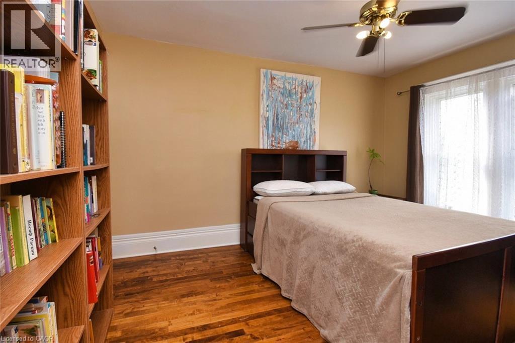 Hardwood flooring with a built-in bookcase, ceiling fan with integrated lighting, and a large window with sheer and blackout curtains - 522 Aberdeen Avenue, Hamilton, ON - Indoor Photo Showing Bedroom