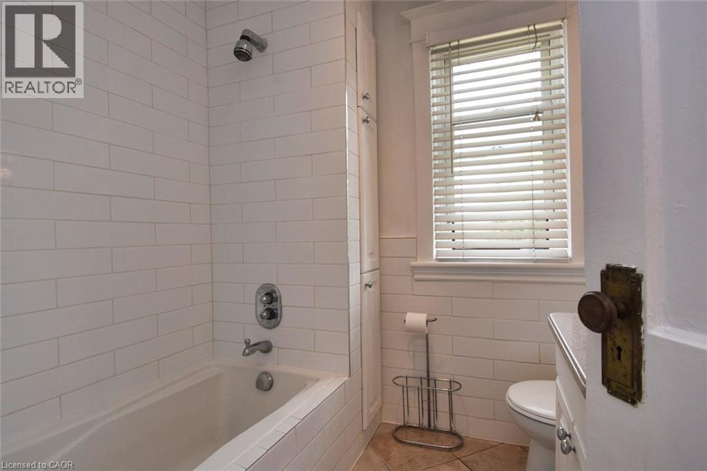 Bathroom featuring a tiled shower/tub combination with chrome fixtures, a window with horizontal blinds, built-in storage cabinetry, and a white commode - 522 Aberdeen Avenue, Hamilton, ON - Indoor Photo Showing Bathroom