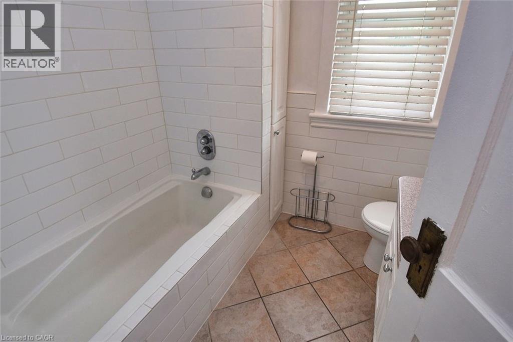 White subway tile surrounding a built-in bathtub with chrome fixtures, complemented by earth-toned square floor tiles - 522 Aberdeen Avenue, Hamilton, ON - Indoor Photo Showing Bathroom