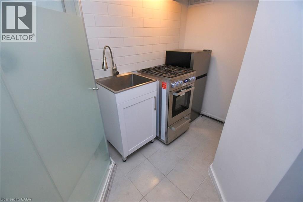 Compact kitchen area featuring a stainless steel sink, gooseneck faucet, white shaker-style base cabinet, and a stainless steel gas range with oven - 522 Aberdeen Avenue, Hamilton, ON - Indoor