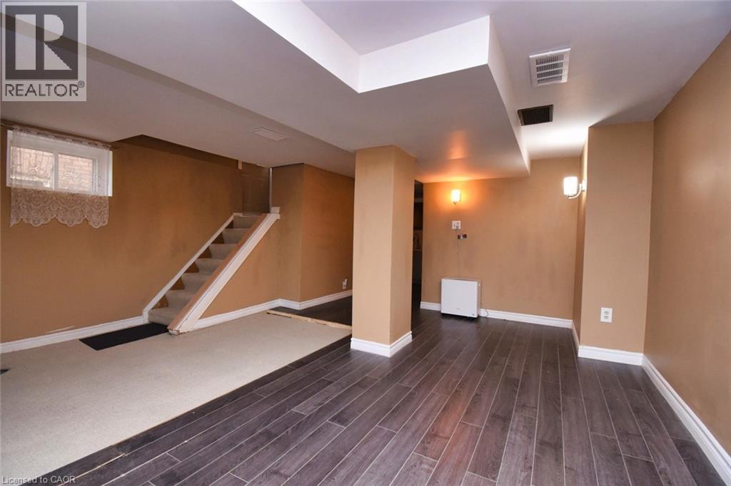 Lower-level room featuring wood-finish flooring, a carpeted stairwell, and a window with brick exterior visible - 522 Aberdeen Avenue, Hamilton, ON - Indoor