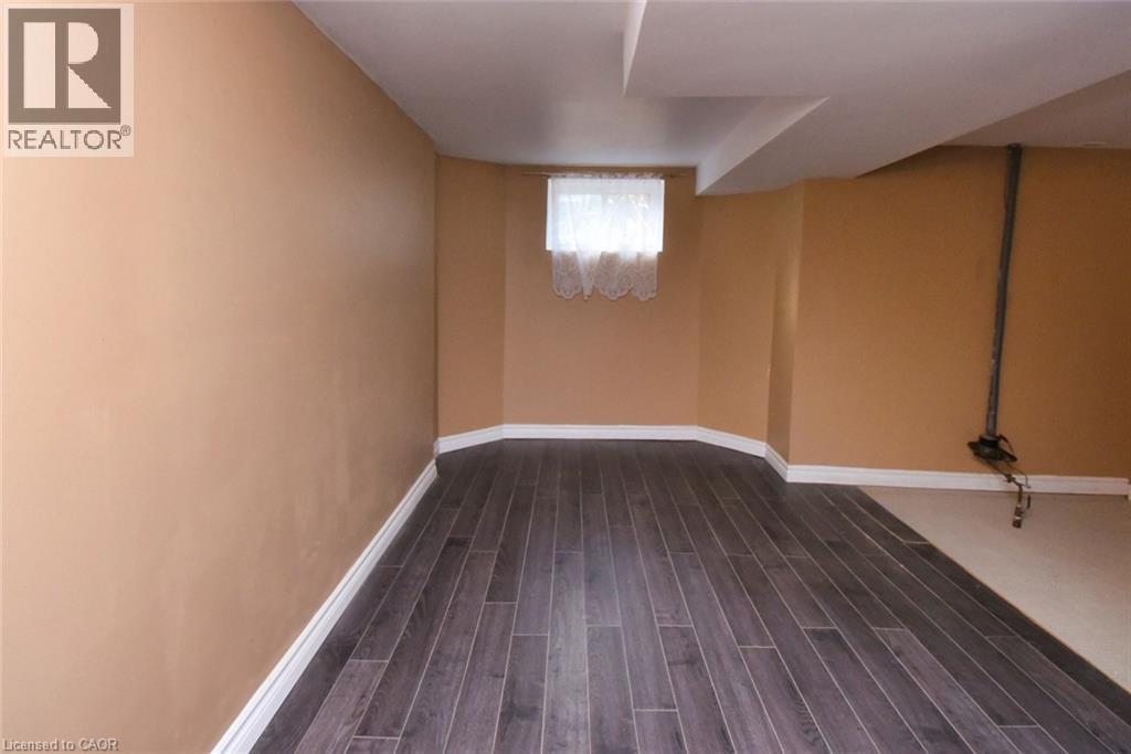 Interior space featuring wood-finish flooring, light tan wall paint, white baseboards, and a window with white curtains - 522 Aberdeen Avenue, Hamilton, ON - Indoor Photo Showing Other Room