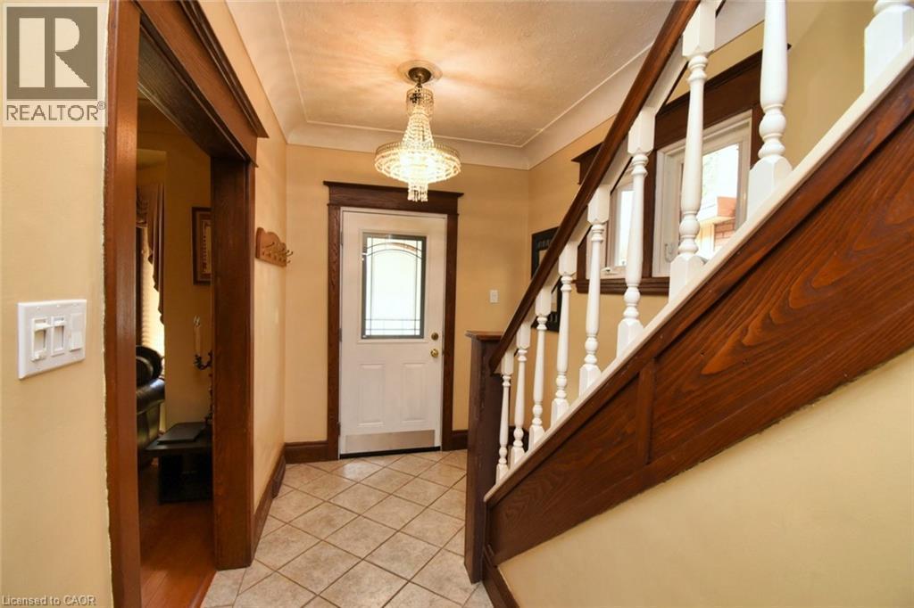 Inviting entryway featuring a crystal chandelier, tiled flooring, a white paneled door with decorative glass, and a traditional wood-finish staircase with white balusters - 522 Aberdeen Avenue, Hamilton, ON - Indoor Photo Showing Other Room