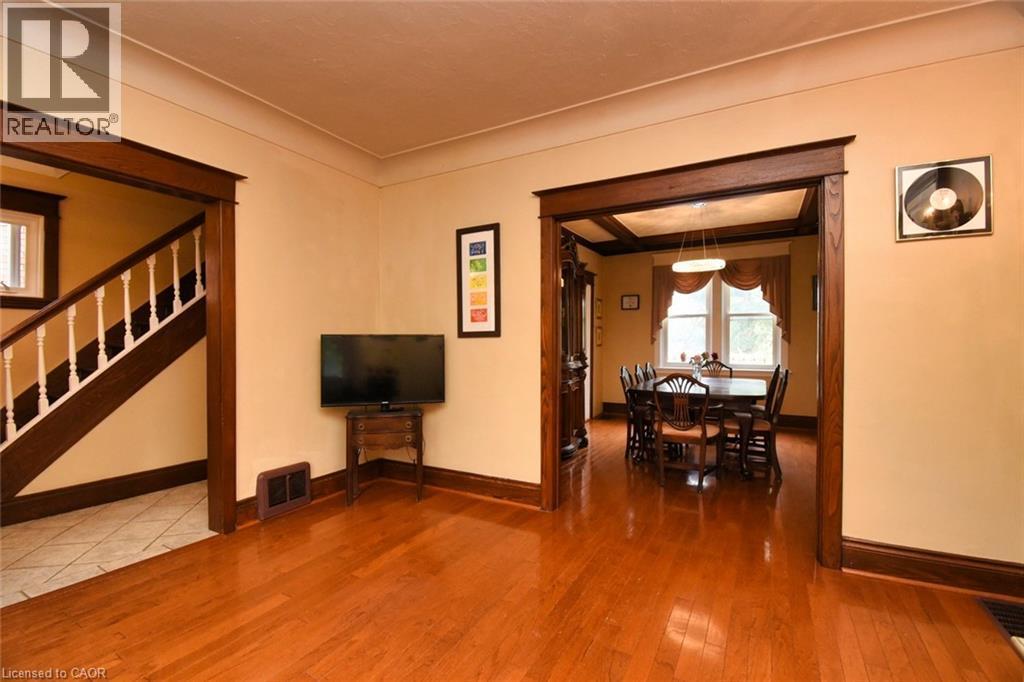 Spacious interior featuring warm wood-finish flooring, substantial dark wood trim, a wide doorway opening, a staircase with white balusters, and a visible dining area with a tray ceiling - 522 Aberdeen Avenue, Hamilton, ON - Indoor Photo Showing Other Room