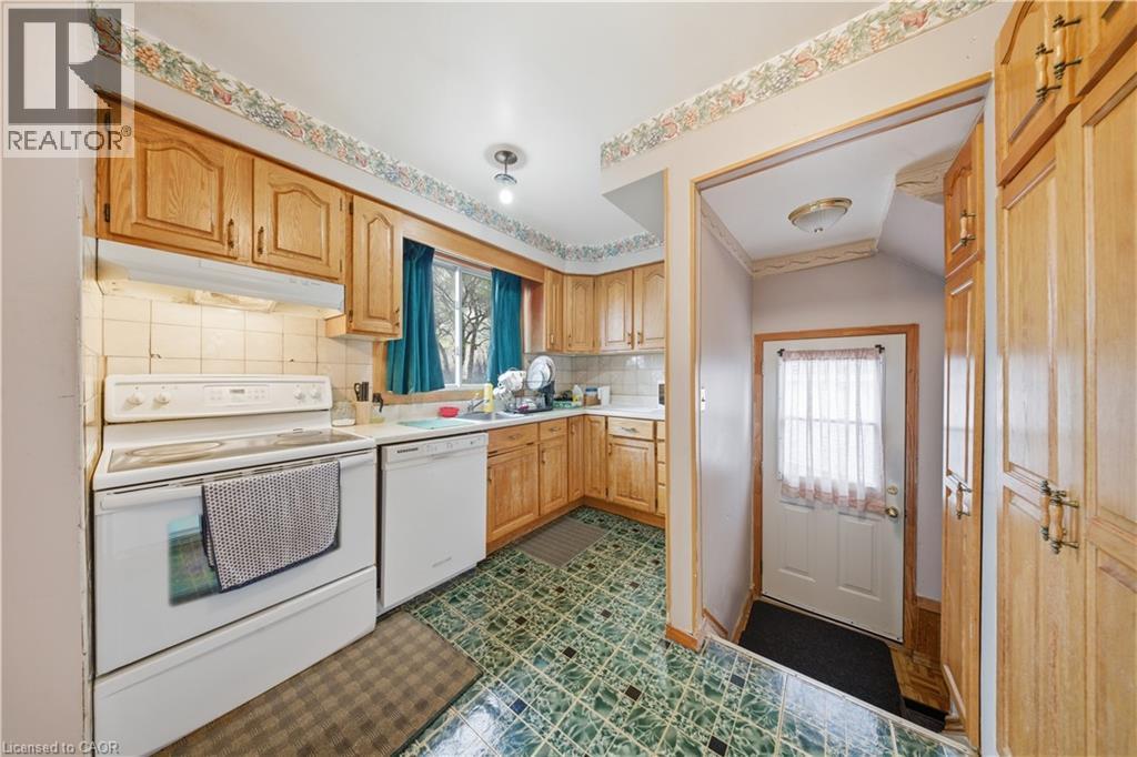 Kitchen featuring wood cabinetry, white appliances, patterned floor tile, and a sink with window - 116 Gainsborough Road, Hamilton, ON - Indoor Photo Showing Kitchen With Double Sink