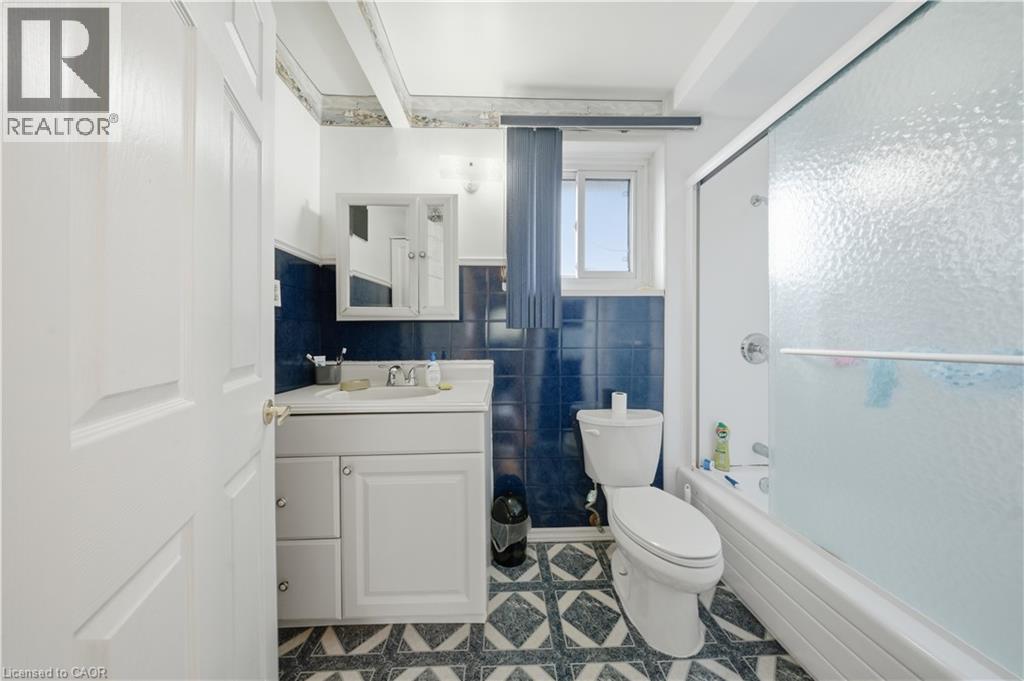 Bathroom featuring a white vanity with integrated sink, chrome faucet, white paneled door, blue tiled walls, and patterned floor tiling - 116 Gainsborough Road, Hamilton, ON - Indoor Photo Showing Bathroom