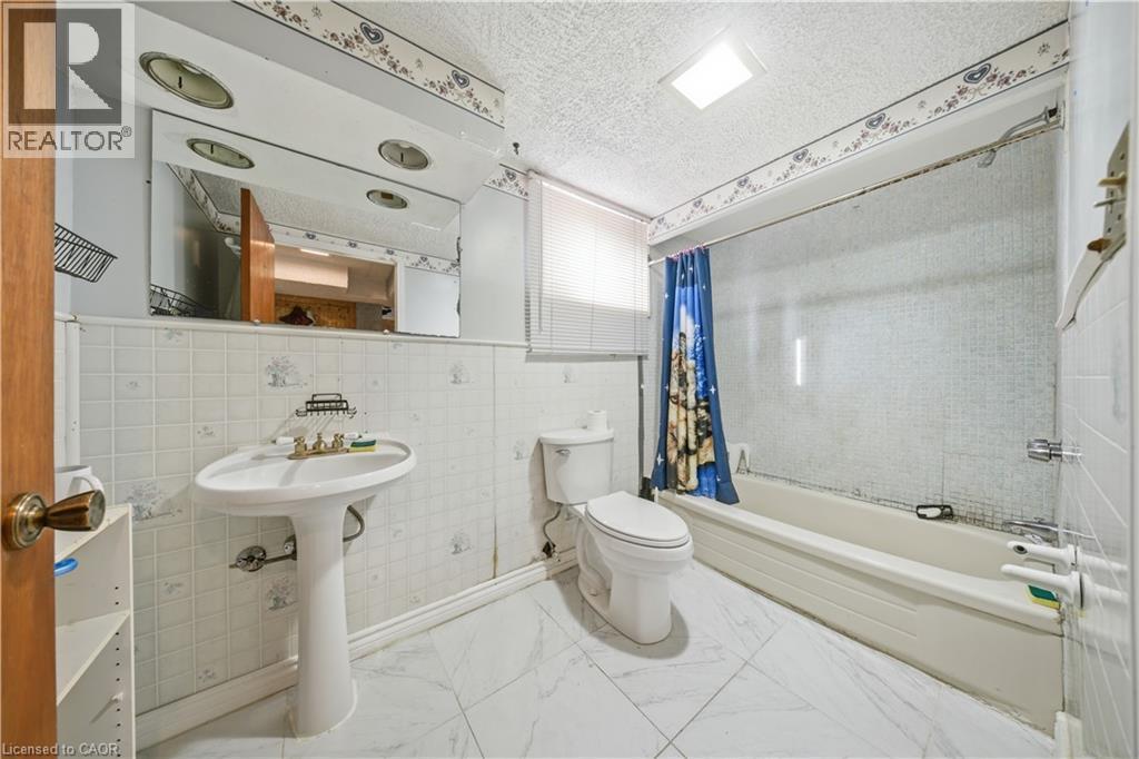 Bathroom featuring a pedestal sink, white tile flooring, a built-in bathtub with shower, and a toilet - 116 Gainsborough Road, Hamilton, ON - Indoor Photo Showing Bathroom