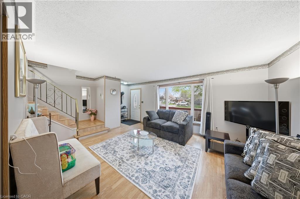 Bright living area featuring wood-finish flooring, a large picture window, and a staircase with an ornamental metal railing - 116 Gainsborough Road, Hamilton, ON - Indoor Photo Showing Living Room