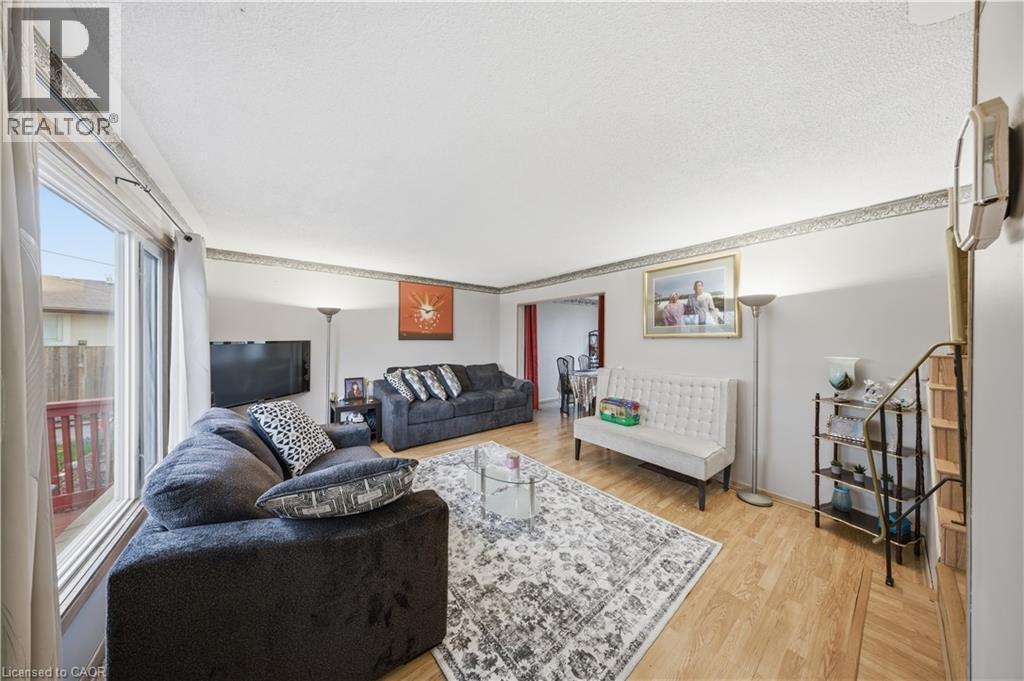 Living area featuring light wood-finish flooring, white walls with decorative border, and a large window providing natural light - 116 Gainsborough Road, Hamilton, ON - Indoor Photo Showing Living Room