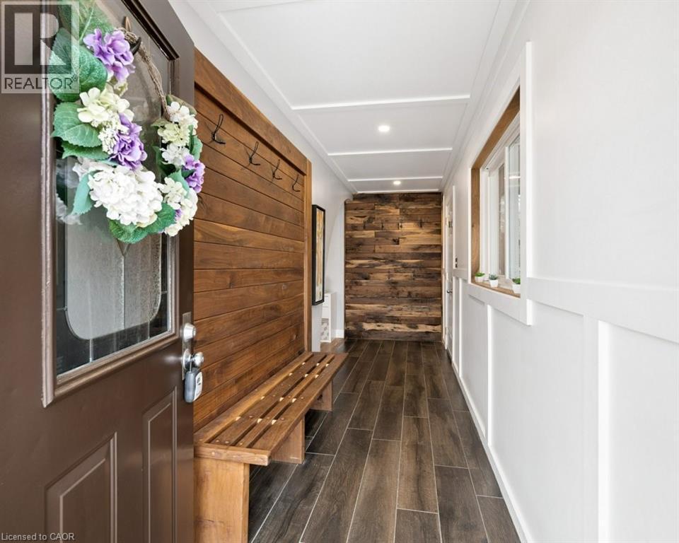 Welcoming entry hall featuring a solid panel door with decorative glass, wood-finish flooring, a built-in wooden bench with coat hooks, and an accent wall with varied wood paneling - 522 Glendene Crescent, Waterloo, ON - Indoor Photo Showing Other Room