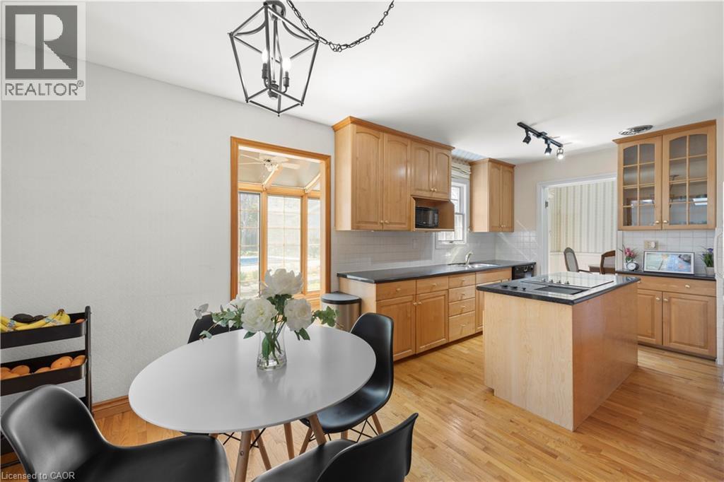 Kitchen featuring natural wood cabinetry, dark countertops, a central island with cooktop, light wood-finish flooring, and a large bay window - 277 Blackacres Boulevard, London, ON - Indoor