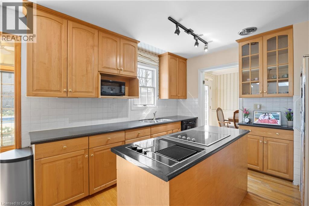 Kitchen featuring light wood cabinetry, white tile backsplash, dark countertops, and a central island with a built-in cooktop - 277 Blackacres Boulevard, London, ON - Indoor Photo Showing Kitchen