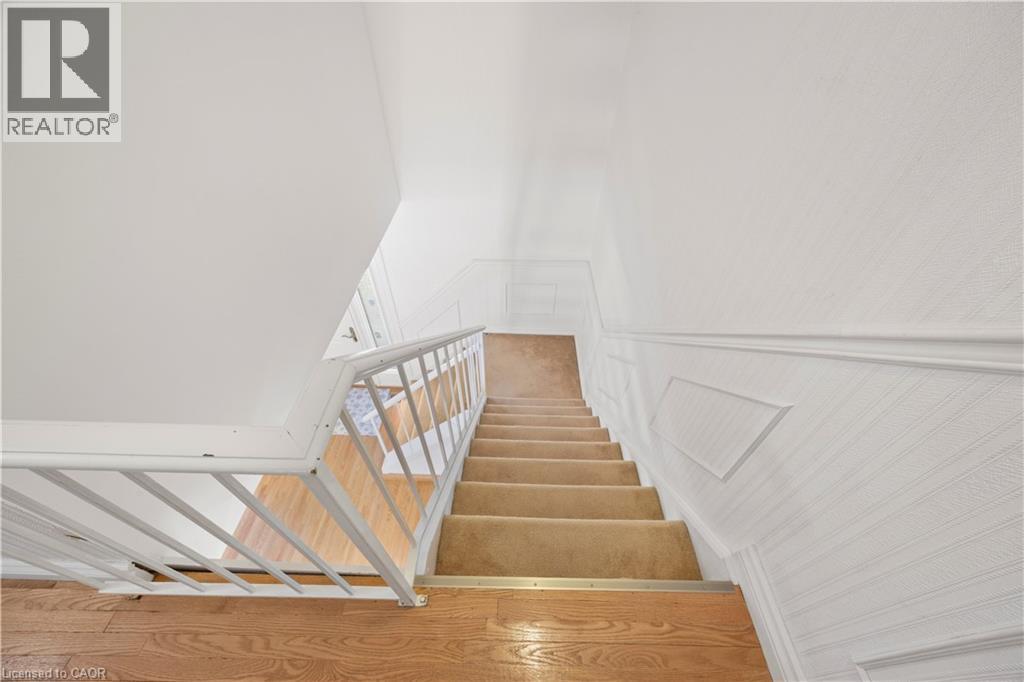 Staircase featuring carpeted treads, wood-finish flooring at the landing, a white metal balustrade, and textured wall finishes with chair rail detailing - 277 Blackacres Boulevard, London, ON - Indoor Photo Showing Other Room