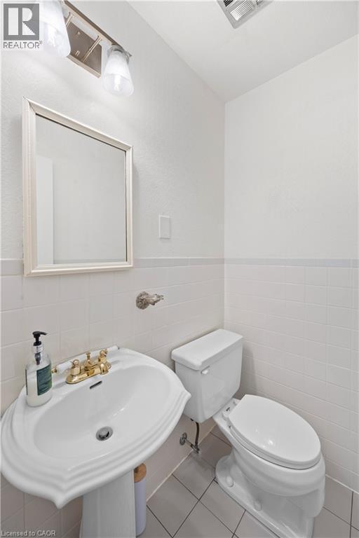Bathroom featuring a pedestal sink with brass-finish fixtures, white tile flooring, white tiled walls, and a wall-mounted mirror - 277 Blackacres Boulevard, London, ON - Indoor Photo Showing Bathroom