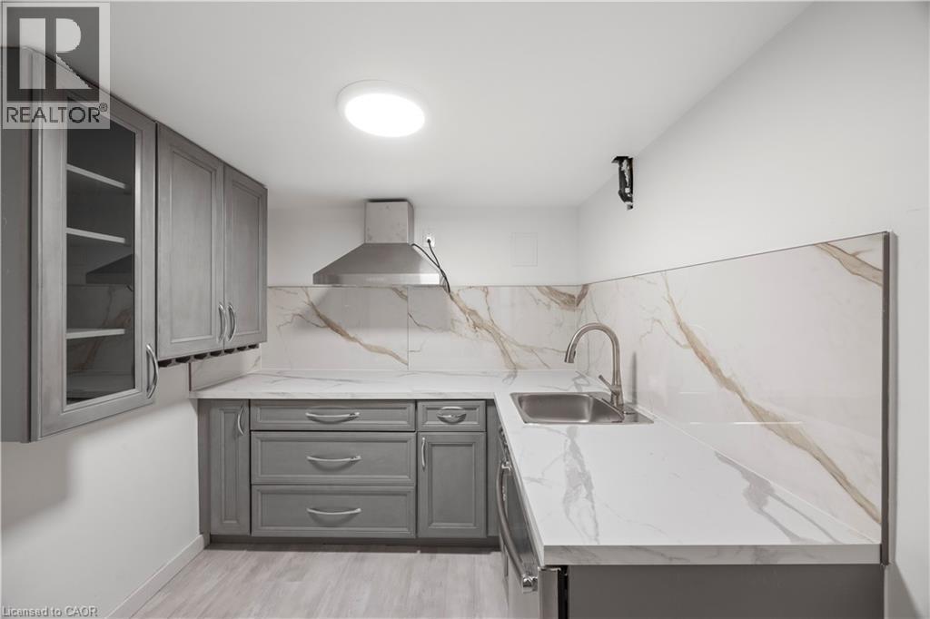 Kitchenette featuring light gray cabinetry, a stainless steel range hood, stone-finish countertops, a matching backsplash, and wood-finish flooring - 277 Blackacres Boulevard, London, ON - Indoor
