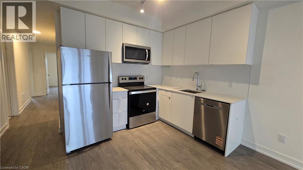 Modern kitchen featuring white cabinetry, stainless steel appliances, light-toned countertops, and wood-finish flooring - 16 Melbourne Avenue Unit# 210B, St. Catharines, ON - Indoor Photo Showing Kitchen With Stainless Steel Kitchen
