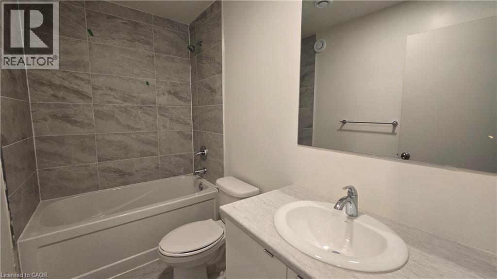 Bathroom featuring a white bathtub with tile surround, a built-in vanity with an undermount sink, a stone-finish countertop, and a large wall-mounted mirror - 16 Melbourne Avenue Unit# 210B, St. Catharines, ON - Indoor Photo Showing Bathroom