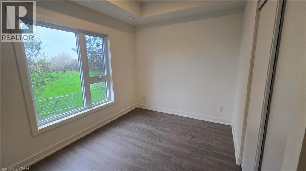 Room featuring a large window, dark wood-finish flooring, white baseboards, and a built-in sliding door closet - 16 Melbourne Avenue Unit# 210B, St. Catharines, ON - Indoor Photo Showing Other Room