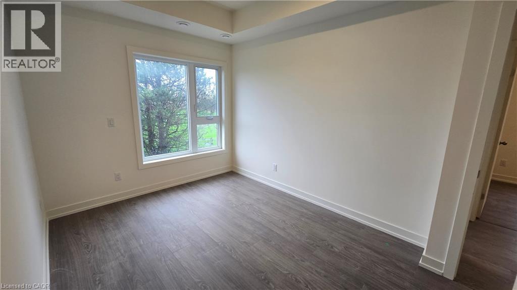 Room featuring a large picture window, wood-finish flooring, white walls, recessed ceiling lighting, and crisp white baseboards - 16 Melbourne Avenue Unit# 210B, St. Catharines, ON - Indoor Photo Showing Other Room
