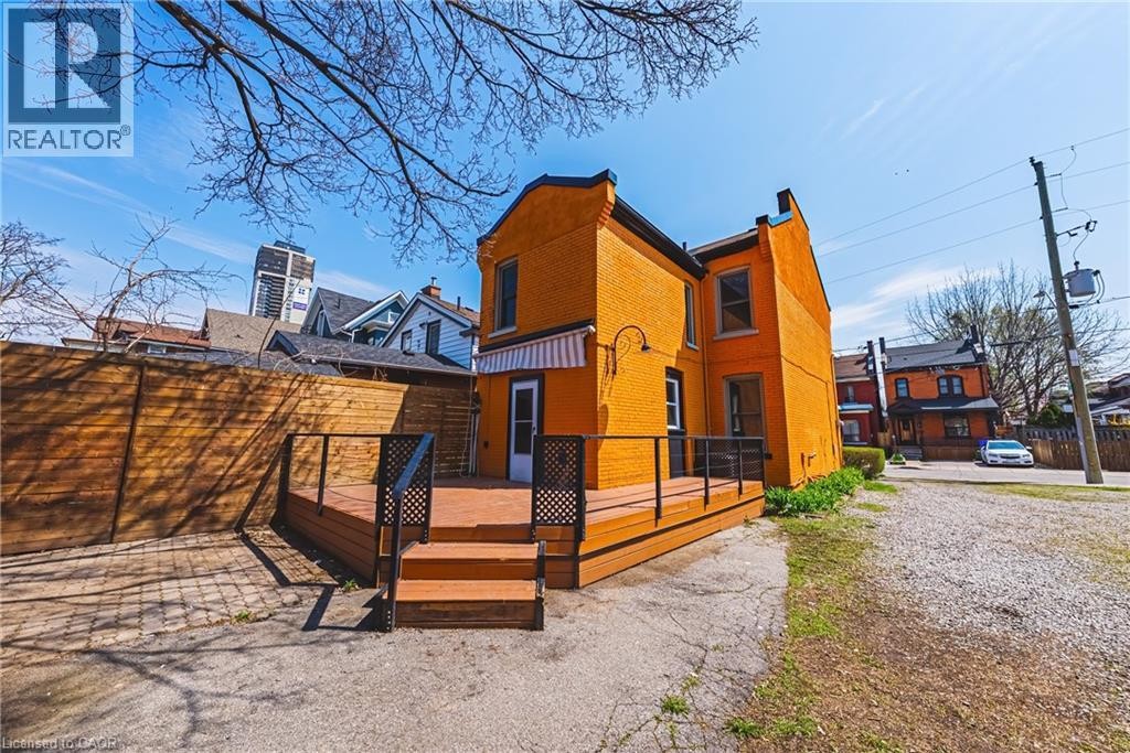 Exterior featuring an expansive wood-finish deck with steps, black railings, and a white and orange striped awning - 116 Catharine Street S, Hamilton, ON - Outdoor