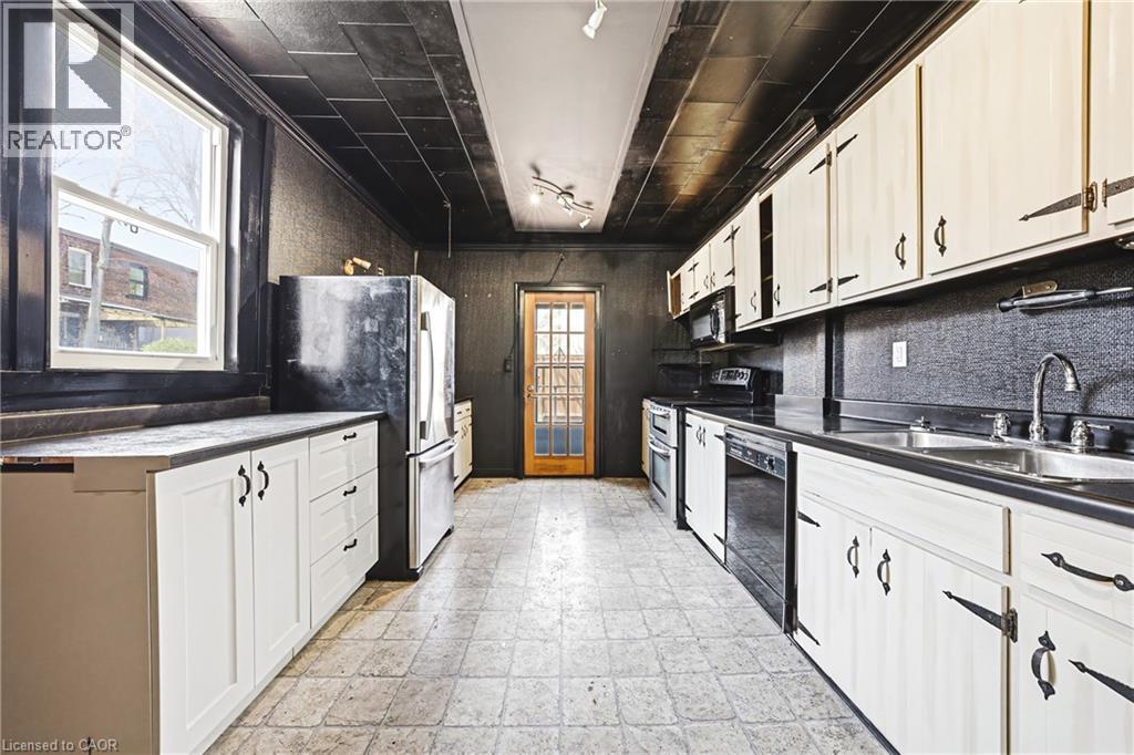 Galley kitchen featuring white cabinetry, black countertops, and a full suite of appliances including a refrigerator, dishwasher, and range - 116 Catharine Street S, Hamilton, ON - Indoor Photo Showing Kitchen With Double Sink
