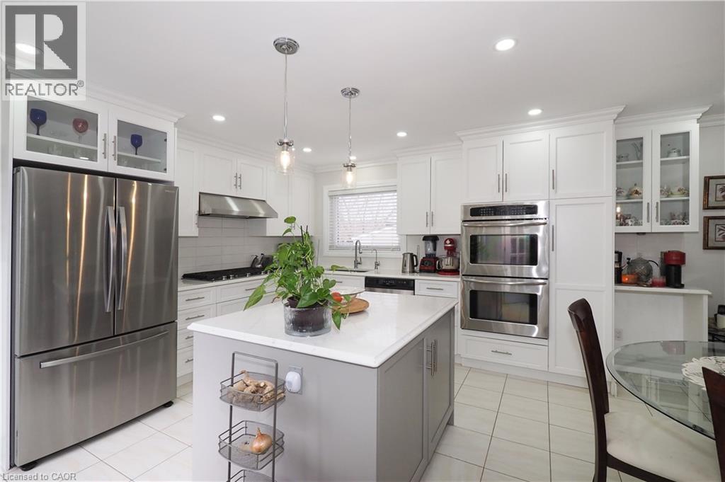 Dual tone kitchen with glass fronted cabinets, stainless steel appliances, a center island, decorative light fixtures, and backsplash - 89 Lynnhaven Court, Kitchener, ON - Indoor Photo Showing Kitchen With Upgraded Kitchen