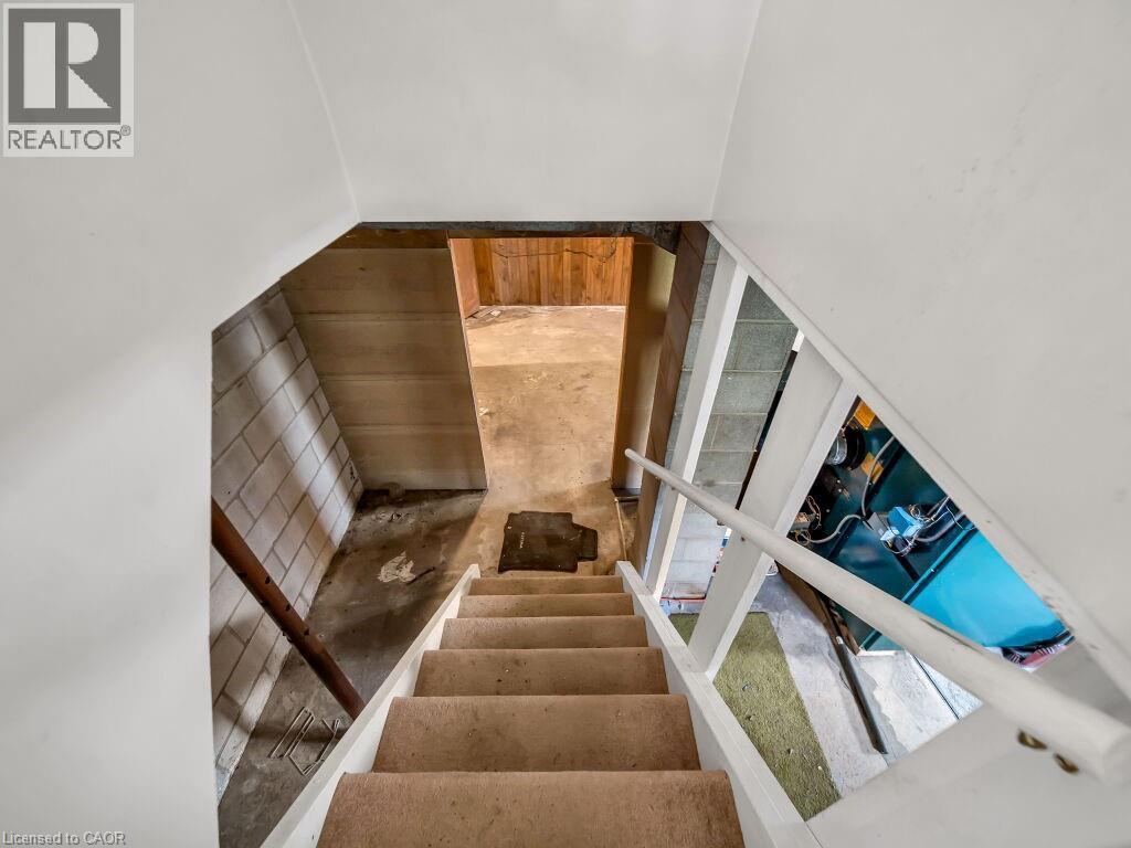 Staircase with carpeted treads, white painted stringers, and a white handrail leading to a lower level featuring exposed concrete block walls and a concrete floor - 1416 Highway 6, Hamilton, ON - Indoor Photo Showing Other Room