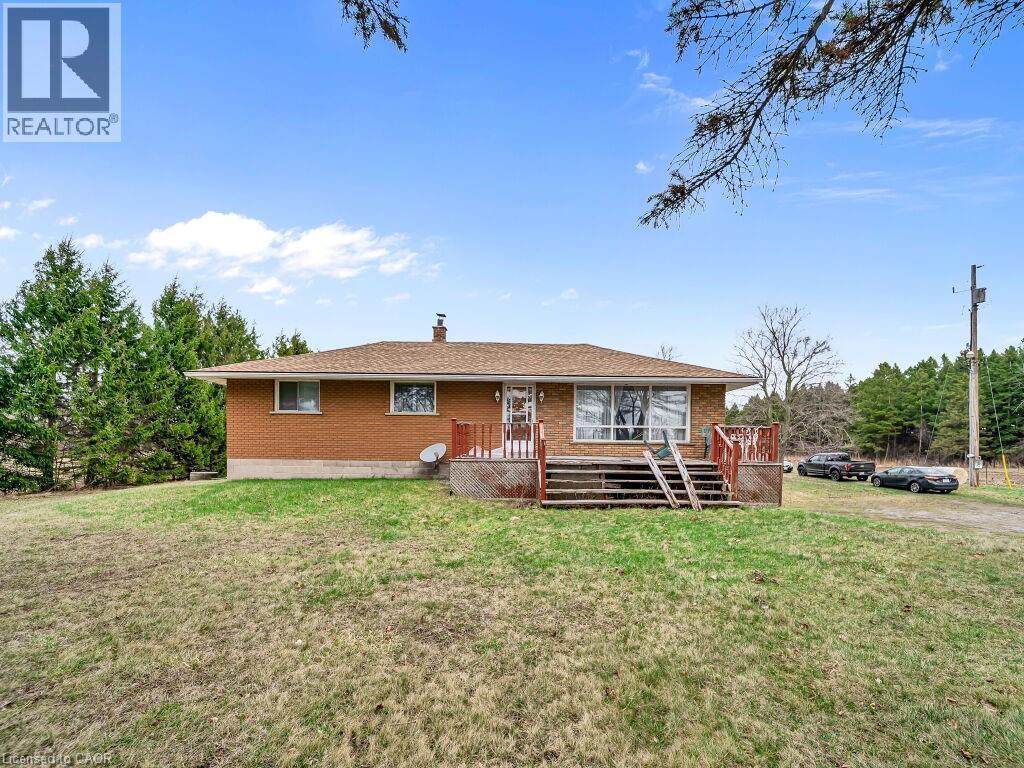 Brick exterior residence featuring a brown shingle roof, a front porch with wood railings, and a gravel driveway - 1416 Highway 6, Hamilton, ON - Outdoor