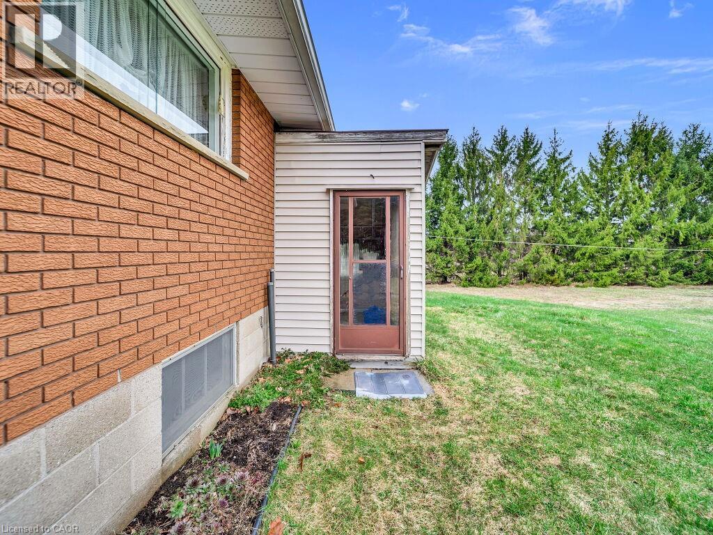 Brick exterior with a window well, a privacy screen of mature trees, and a side entry with a glass-paneled door - 1416 Highway 6, Hamilton, ON - Outdoor With Exterior