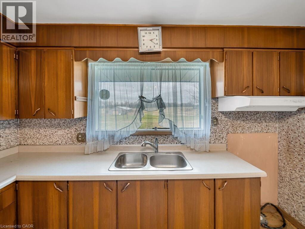 Kitchen featuring a double basin stainless steel sink, laminate countertops, wood-finish cabinetry, and a mosaic tile backsplash - 1416 Highway 6, Hamilton, ON - Indoor Photo Showing Kitchen With Double Sink