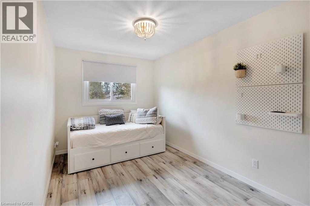 Bright room featuring a window with roller shade, wood-finish flooring, and a decorative ceiling light fixture - 32 Montclair Crescent, Simcoe, ON - Indoor Photo Showing Bedroom