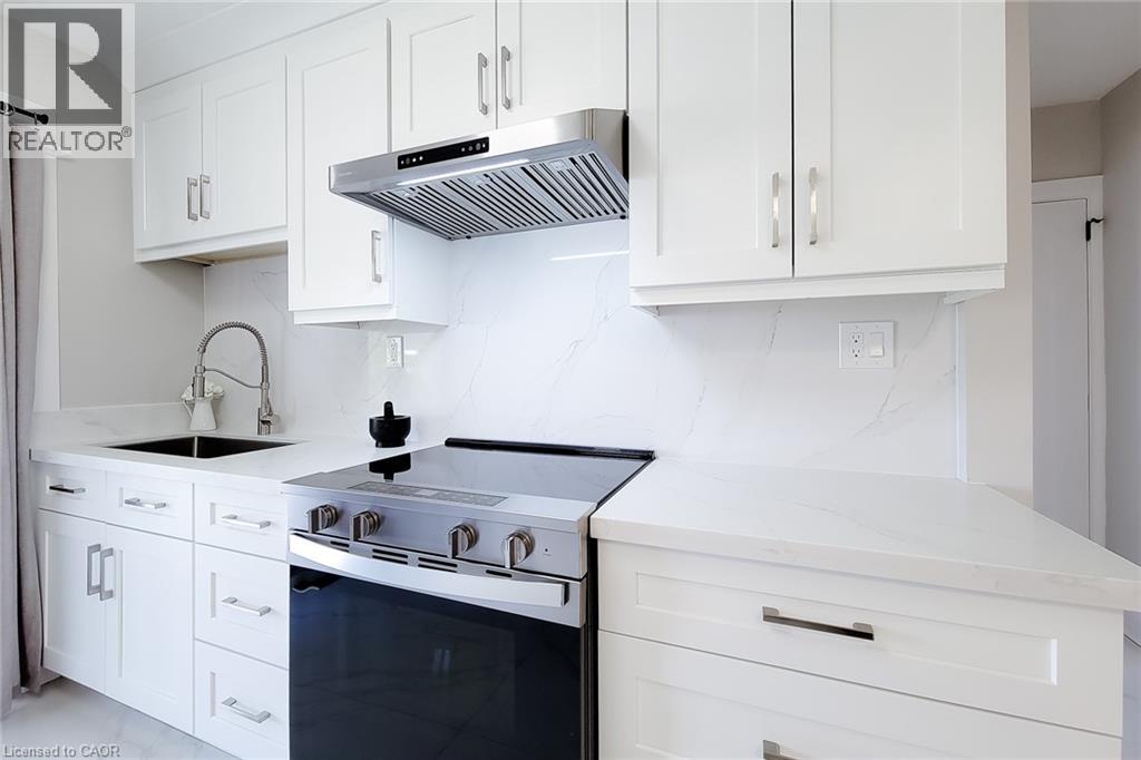 White shaker cabinetry with brushed nickel hardware, stainless steel range with overhead ventilation, undermount sink with gooseneck faucet, and stone countertops extending to a full-height backsplash - 103 East 45Th Street, Hamilton, ON - Indoor Photo Showing Kitchen With Upgraded Kitchen